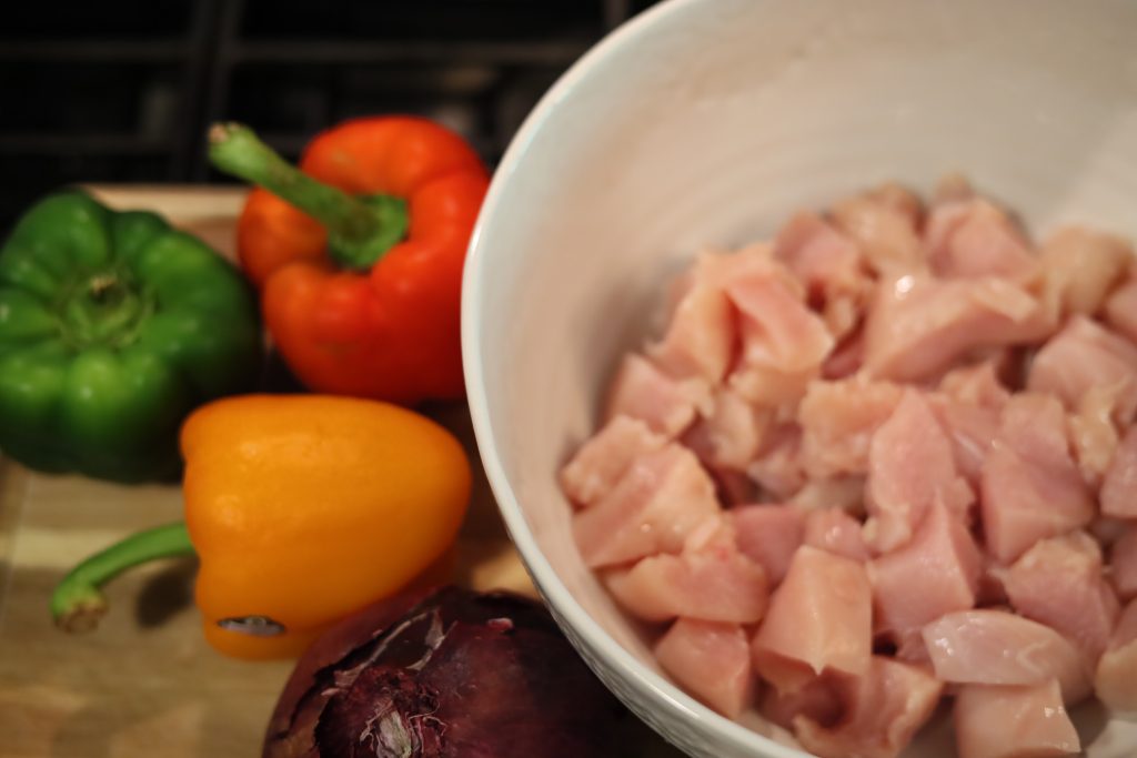 bowl of diced raw chicken and raw bell peppers and onion 