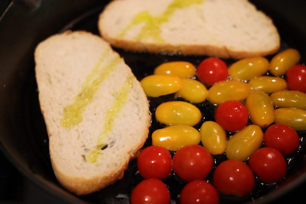 two slices of grilled bread and colorful tomatoes grilling in a pan